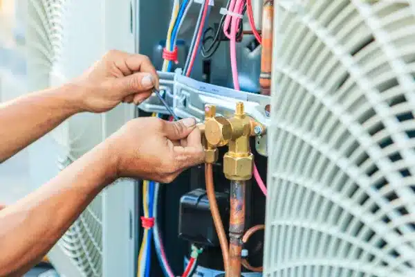 Person working on an air conditioning unit, using tools to adjust wires and pipes.