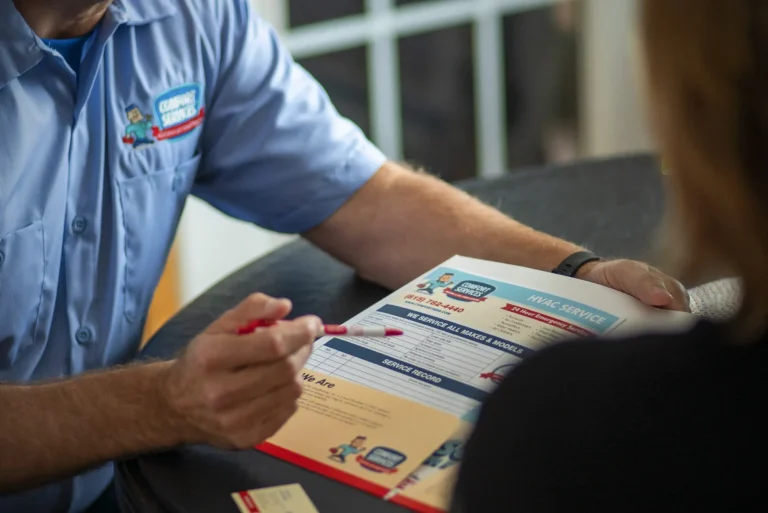 Person in a blue uniform discusses HVAC service brochure with another individual at a table.